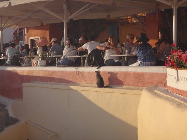 Pessoas confortavelmente instaladas no restaurante aguardando pelo pôr do Sol em Oia.