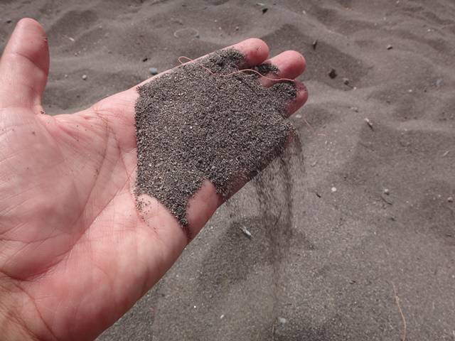 A praia tem essa areia grossa e escura, antes da camada de pedras.